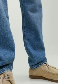 Blaue Jeans aus Baumwolle mit geradem Schnitt und leicht ausgefranstem Saum. Kombiniert mit hellbeigen Wildlederschuhen mit Schnürsenkeln und einem niedrigen Absatz.