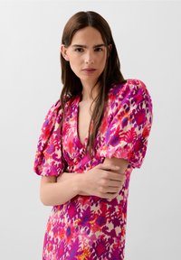 Farverig omviklingskjole med et blomster mønster i nuancer af pink, lilla og hvid. Korte puffærmer og en dyb V-hals design.