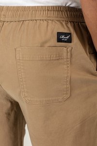 Pantalones cortos color caqui con cinturilla elástica, que cuentan con un bolsillo trasero de parche y una etiqueta de marca negra con texto blanco en el bolsillo.