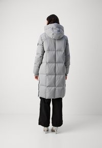 Grijze gewatteerde pufferjas met een capuchon, lange mouwen en zijritsen, gecombineerd met zwarte broeken en gepatternde schoenen.