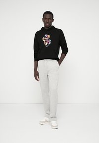 Felpa nera con un grafico di un orsetto colorato, abbinata a pantaloni della tuta grigi chiari e sneakers bianche. Design semplice e casual.