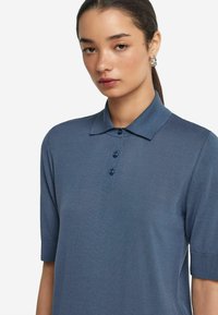 Mörkblå pikétröja i slät tyg med korta ärmar, krage och tre matchande knappar fram.