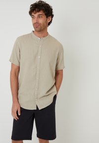 Camisa beige de manga corta con cuello alzado, hecha de una tela texturizada, combinada con pantalones cortos azul marino oscuros.