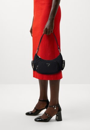 Black nylon handbag with dual zippered sections, silver hardware, and a triangular logo. Patent leather heels with ankle straps. Red textured dress.