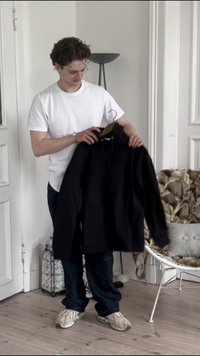 Black hoodie with a drawstring, held by a person in a white t-shirt. Soft fabric, long sleeves, relaxed fit. Minimalistic design.
