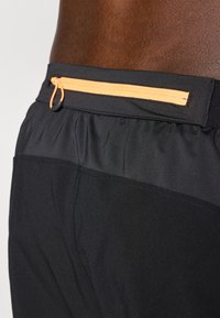 Black athletic shorts with a smooth texture, featuring a secure black waistband and an orange zippered pocket on the back.