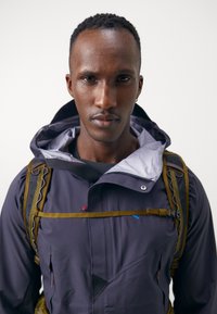 Water-resistant, dark purple jacket with a hood, featuring a zipper, geometric design, and textured accents. Equipped with a backpack.