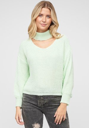 Light mint green knitted sweater with a high neck, wide sleeves, and v-neck cut. Features ribbed texture and hemline. Paired with distressed jeans.