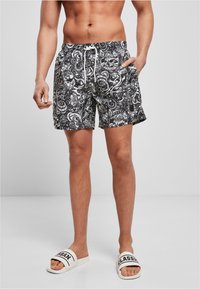 Schwarz-weiße gestreifte Badehose mit elastischem Bund und Kordelzug, ausgestattet mit Seitentaschen und einem strukturierten Stoff.