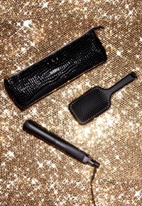 Zwarte opslagcase met krokodillenpatroon, matte zwarte paddleborstel met rubberen grip, en stijlvolle zwarte haarstijlstaaf met snoer, allemaal op een sprankelende achtergrond.