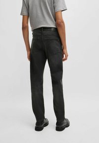 Jeans de mezclilla negra con un corte recto, que cuentan con dos bolsillos traseros y un ligero desgaste. Combinados con una camiseta gris y zapatos negros.