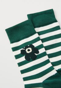 Chaussettes rayées vertes et blanches avec un poignet côtelé ornées d'un motif de fleur noire. Fabriquées en tissu doux avec une texture lisse.