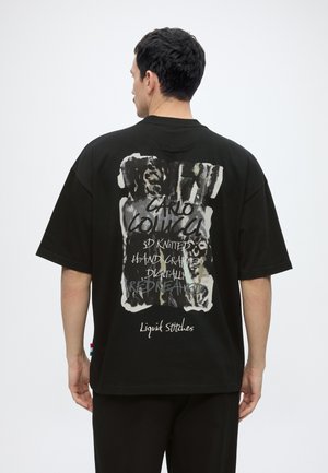 Mann von hinten trägt schwarzes Oversize-T-Shirt mit abstraktem Design und dem Schriftzug "Carlo Colucci 3D Knitted Hand Crafted Digitally Redreamed Liquid Stitches."