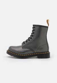 Bota de cuero negro con superficie texturizada, puntera redonda, diseño con ocho ojales para cordones, costuras amarillas en contraste y una lengüeta en el talón.