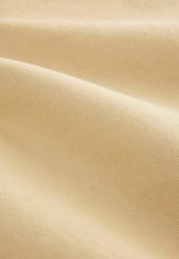 Puuvillakangas vaaleanbeigessä värissä, jossa on hieno, teksturoitu kudos, esittäen pehmeää, sileää pintaa ja hienovaraista kiiltoa. Joustava ja laskeutuu hellästi.