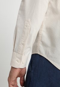 Lichtgekleurde lange mouwen overhemd met knoopmanchetten en een schuine zoom; de stof lijkt zacht met een lichte textuur en stiksel detail.