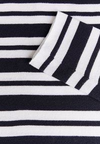 Tessuto a maglia a righe blu navy e bianche con larghezze di strisce variabili; superficie liscia; dettaglio della manica piegata visibile.