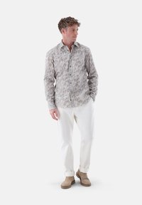 Long-sleeve shirt in light beige with intricate paisley pattern. Paired with white trousers and beige ankle boots, featuring rolled cuffs.