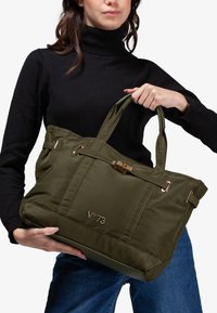 Borsa tote in nylon verde oliva con dettagli in oro, doppie maniglie e chiusura a scatto. Presenta un logo embossato sul fronte.