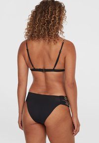 Svart bikini med et enkelt design, som har tynne justerbare stropper og intrikate gullbladdetaljer på sidene av trusa. Glatt tekstur.