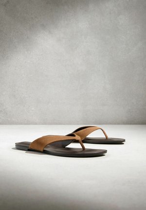 Sandale din piele întoarsă maro, cu talpă plată neagră, așezate pe o suprafață gri deschis, cu un fundal texturat gri.