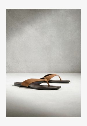 Sandale din piele întoarsă maro, cu talpă plată neagră, așezate pe o suprafață gri deschis, cu un fundal texturat gri.