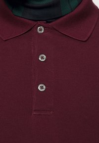 Bordeaux polo tričko vyrobené z texturované tkaniny se třemi stříbrnými knoflíky, s klasickým límcem a designem skryté légy.