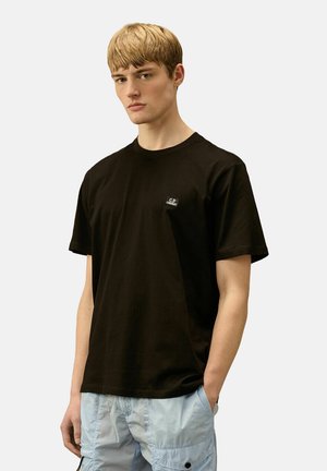 T-shirt nera in cotone con maniche corte, scollo a girocollo e piccolo logo ricamato sul lato sinistro del petto. Il modello indossa pantaloni cargo azzurri chiari.
