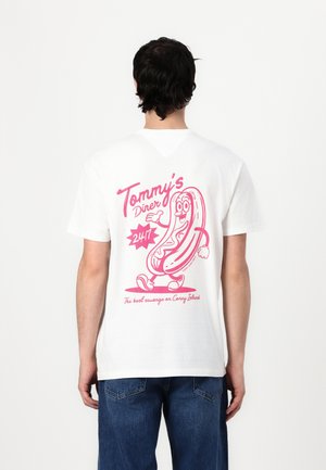 Bijela pamučna majica s velikim ružičastim grafičkim prikazom crtanog hot doga i natpisom "Tommy's Diner 24/7" s dodatnim sloganom ispod.