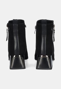 Botas negras hasta el tobillo con parte superior de ante, detalles de cuero, cierre de cremallera y un tacón metálico grueso con un diseño texturizado.