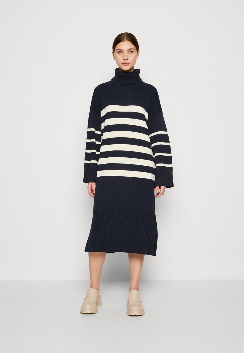 Niebiesko-kremowa sukienka swetrowa w paski z wysokim golfem, prążkowanymi mankietami i prążkowanym dołem, z bocznymi rozcięciami dla łatwości ruchu.