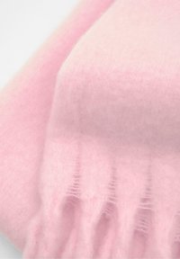 Světle růžový vlněný šátek s měkkým, texturovaným povrchem. Má třásňové okraje a hladký povrch.