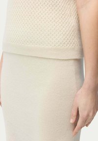 Stickad krämfärgad tröja med strukturerat diamantmönster; sömlös övergång till en slät, åtsittande krämfärgad kjol. Mjuk, enhetlig tyg.