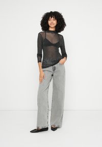 Čierny, priesvitný top s dlhými rukávmi a trblietavým textúrou, skombinovaný s voľnými, vysoko pásovými sivými džínsami a čiernymi balerínkami. Jednoduchý, moderný dizajn.