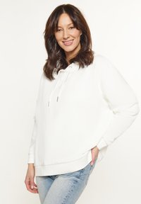 Witte hoodie met trekkoord, relaxte pasvorm, ribbelmanchetten en -zoom; gecombineerd met lichtblauwe jeans. Gelijke textuur, eenvoudig ontwerp.