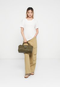 White short-sleeve shirt, khaki cargo pants with pockets, olive green handbag with star accent, and patterned shoes with a flat sole.