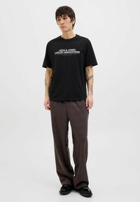 Svart bomullströja med vit textlogga "JACK & JONES LUXURY INNOVATIONS" kombinerad med bruna rutiga byxor och svarta skor.