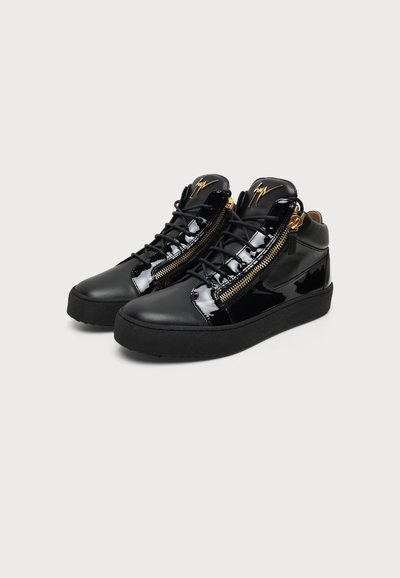 Μαύρα sneakers με ψηλό πάνω μέρος, γυαλιστερές πατέντες, χρυσά πλαϊνά φερμουάρ, μαύρα κορδόνια και χρυσλό λογότυπο υπογραφής στη γλώσσα, εμφανίζονται σε λευκό φόντο.