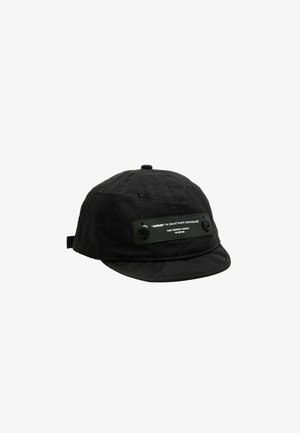 Gorra negra hecha de tela texturizada, con visera plana, detalles en botones y una etiqueta rectangular en la parte frontal con texto en blanco.