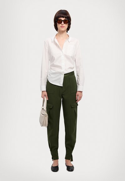 Weißes Hemd mit Knöpfen, olivgrüne Cargo-Hosen mit Seitentaschen, schwarze Ballerinas und eine beige Handtasche. Die Person trägt dunkle Sonnenbrillen.