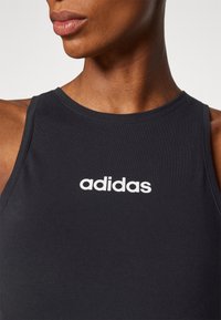 Juodas be rankovių sportinis marškinėlis, pagamintas iš tamprios medžiagos, su apvaliu iškirpimu ir baltu "adidas" logotipu per krūtinę.