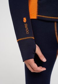 Marineblå og orange termisk langærmet top med tommelhul, der har kontrasterende syninger og et lille logo på ærmet. Blød tekstur.