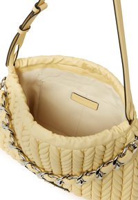 Sac à main jaune tissé avec une texture douce, poche intérieure et accents en chaîne argentée. La bandoulière présente un bord noir contrastant.