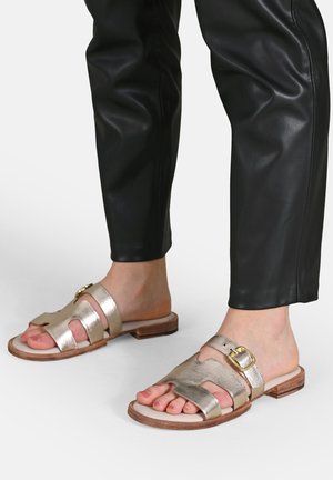 Metallisch goldene Rutschsandalen mit offener Zehenpartie, ausgestattet mit zwei erhöhten Riemen und einer Schnalle. Holzhüf und lederartiger Textur.
