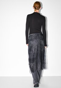 Mustapaita, jossa on pitkät hihat, yhdistetty tummaan farkkuhousuihin ja läpikuultavaan mustaan pitsihameeseen, jossa on kukkakuvioita ja virtaava muotoilu.