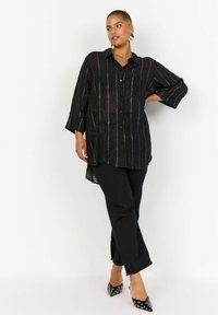 Fekete, gombos ing átlátszó anyagból, függőleges, irizáló csíkokkal. Bokáig érő fekete nadrág és ezüst részletekkel ellátott, hegyes fekete cipők.