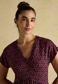 Blumenkleid mit navy Hintergrund, das pinke und grüne Blumenmuster aufweist, kurze Ärmel und ein V-Ausschnitt-Design hat. Weicher Stoff.