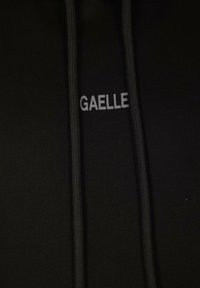 Felpa nera con cappuccio e coulisse. Sul davanti presenta la parola "GAELLE" in bianco, centrata, con una texture di tessuto liscia.