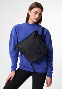 Schwarze Nylon-Crossbody-Tasche mit Reißverschluss, verstellbarem Gurt und Vordertasche. Glatte Textur und minimalistisches Design.