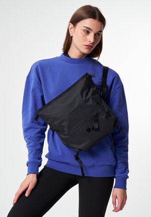 Zwarte nylon schoudertas met ritssluiting, verstelbare schouderband en voorvak. Glad textuur en minimalistisch ontwerp.